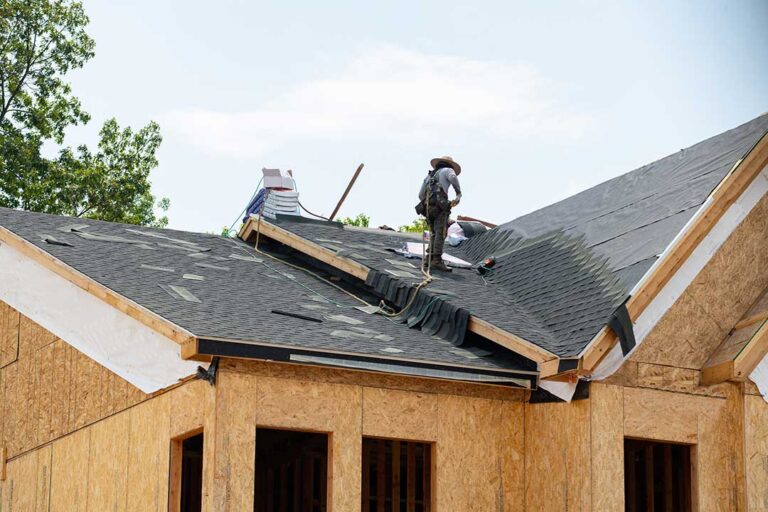 A homeowner using binoculars to inspect a house roof surrounded by autumn trees.