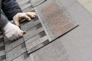 Homeowner in safety gear gently cleaning a shingle roof with a soft brush on a clear day.