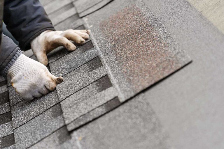 Homeowner in safety gear gently cleaning a shingle roof with a soft brush on a clear day.