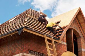 Homeowner inspecting roof shingles from the ground beside a ladder, gutters, and fallen leaves.