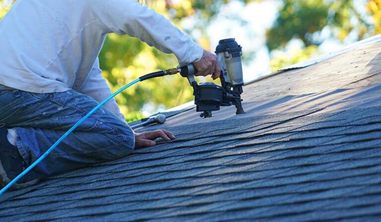 Inspector examining roof shingles beside a ladder while another person reviews notes near a home.